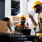 African american logistics managers team dicussing goods distribution at warehouse reception. Post office men and woman workers planning stock supply while chatting at counter desk