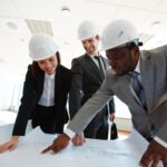 Confident architects in protective helmets looking at blueprint